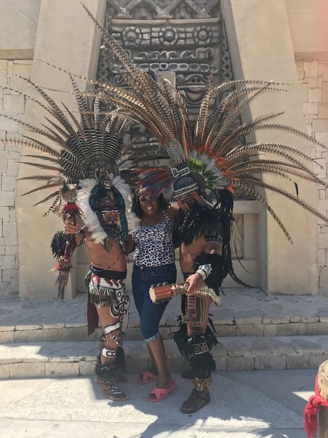 Freddie posing with Aztec dancers in feathered regalia in front of a stone pyramid