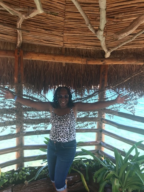Freddie with arms outstretched inside a thatched-roof beach hut by the sea